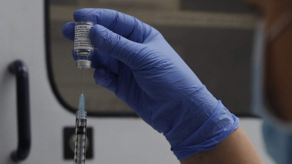 An image depicting a vaccine vial and syringe on a table with a blurred background